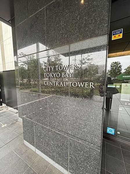 ダークグレーの石張りの壁面に金属製の英字文字が施された館銘板が目を引くエントランスで、足元にはフラットなタイルが敷かれ、ガラス張りの風除室へと続いています。