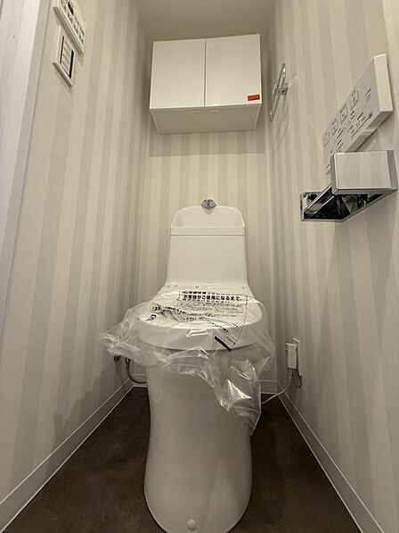 【トイレ】ストライプ柄のクロスがおしゃれなトイレ。温水洗浄便座付きで毎日快適に使うことができます。トイレットペーパーのストック置きに便利な収納付き。