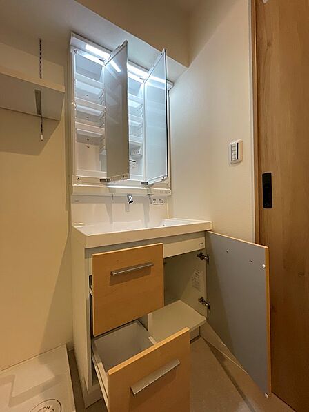 洗面台には三面鏡収納を設置。化粧品や洗面用具をすっきり整理できます。足元収納も備え、タオルなどのストックも十分に収納可能です。