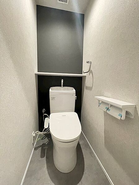 壁の一部にアクセントクロスを採用した、落ち着いた雰囲気のトイレ。手洗いボウルと収納棚を設置し、機能性にも配慮しました。