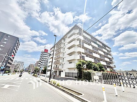 陽光を浴びて輝く、白を基調としたスタイリッシュな大規模マンション。敷地周囲の豊かな植栽が建物を包み込み、街並みに調和した心地よい住環境を作り出しています。