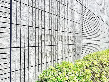凹凸感が重厚な割り肌調タイルに掲げられた「シティテラス板橋蓮根」のステンレス切り文字サイン。青々とした植栽に映える格調高いエンブレムが、住まい手のステータスと所有欲を満たします。