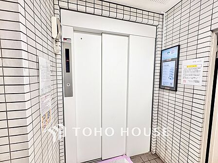 清潔感のある白を基調としたエレベーターホール。壁面には電子掲示板が設置されており、マンション内のお知らせや地域情報を手軽に確認できます。