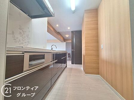 木目調のパネルが温かみを添える、洗練されたデザインのシステムキッチンです。収納スペースもたっぷりと確保されており、調理道具もすっきりと収まります。使い勝手の良さが、日々の料理をさらに楽しい時間に!