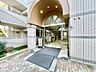 エントランス：緑豊かな植栽とアーチ形状が織りなす開放的で洗練された玄関アプローチですね！清潔感あふれるガラス扉と明るい照明が優しい温もりを添える、心地よい迎賓のエントランス空間！