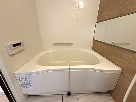 2022年リフォーム済。ゆったりとした浴室は帰宅後の癒しの空間。木目調のアクセントパネル+横長のミラーで温かみと視覚的な広がりを演出しています。