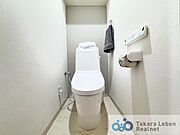 温水洗浄便座付トイレ。サイドには広く見せる白のクロス、正面には柔らかみを持たすグレーを使用。洗面室・トイレの床には汚れを目立ちにくくさせる大理石調を使用しています。
