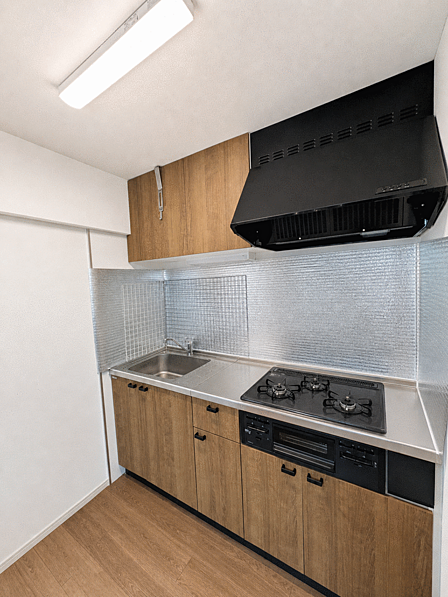 キッチン全体 木目調の扉がやさしい印象のキッチンです。3口ガスコンロとグリル付きで、吊戸棚も備わり調理器具をすっきり収納できます。ご家族のお料理が楽しくなりそうです。