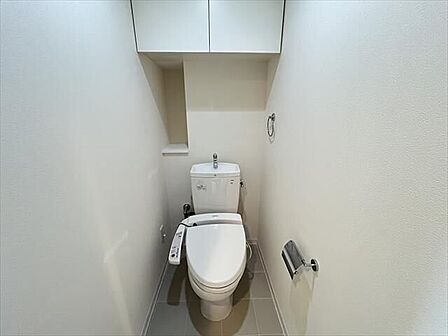 白を基調としたシンプルな壁紙のトイレです。収納棚付きで、トイレットペーパーのストックなど保管できます。棚には小物を置くことができますね♪