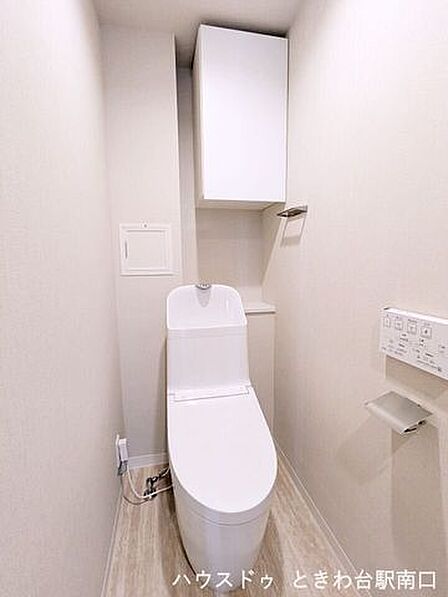 清潔感のある白で統一された温水洗浄便座付きのトイレです。上部には備品の保管に便利な吊戸棚が設置されており、限られたスペースを有効に活用できるすっきりとした設計となっています。