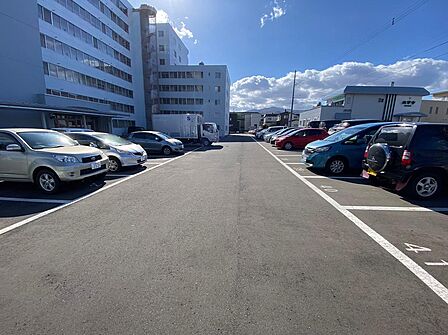 建物前に平置きの駐車区画が並ぶ敷地内駐車場。中央に通路があり、お車の出し入れや建物までの動線を確認できます。車を使う暮らしを想像しながら、区画の広さや空き状況、利用料の条件も見学時にお確かめください。