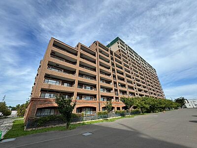 外観：レンガ調の外壁が印象的な、存在感のあるマンション外観。ゆとりある敷地に建ち、落ち着きのある佇まいが魅力です。青空に映える重厚感あるデザインで、住まう方を心地よく迎えてくれる素敵な住まいです。