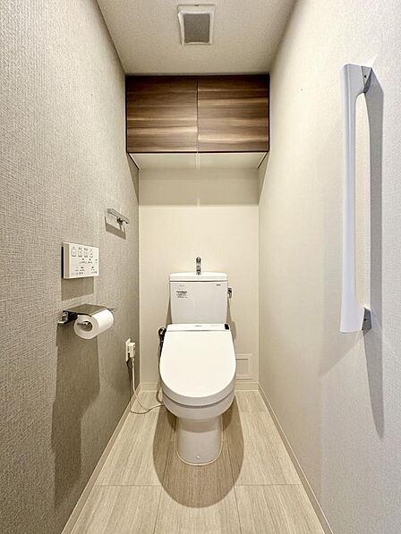 温水洗浄便座付きの機能的なトイレ空間です。上部には棚が設置されているため、トイレットペーパーのストックや清掃用品などを目立たずに収納でき、空間全体をいつでも清潔に保つことができます。