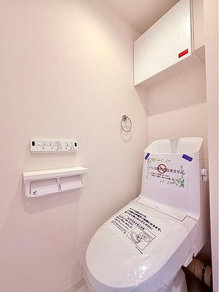 ウォシュレットのついた温水洗浄便座のトイレです。扉付きの吊戸棚もあり、掃除用具や予備のトイレットペーパーなども隠してたっぷり収納できます。壁面のニッチには芳香剤を置いたり、便利にお使いいただけます。