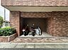 駐車場：重厚なレンガタイルに囲まれた屋根付きのバイク置場。雨風や直射日光から大切な愛車をしっかりと守り、劣化を防ぎます。道路からのアプローチもスムーズで、快適なライディングライフをサポートする設備です。