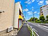 外観：建物前から道路の反対方向を撮影。歩道やガードレール、周辺の住宅街の様子が分かります。