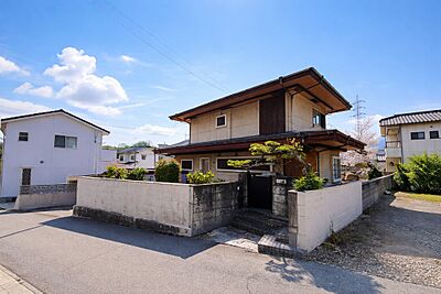 外観：塀に囲まれたプライベート感のある設計で、家族の時間を静かに過ごせるガレージ付きの一戸建て