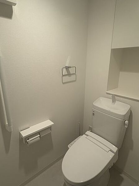 温水洗浄便座付きの清潔なトイレ。上部には棚が設置されており、トイレットペーパーや掃除用具をすっきりと収納できます。シンプルでモダンなデザインは落ち着きがあり、来客時にも好印象を与える清潔な空間です。