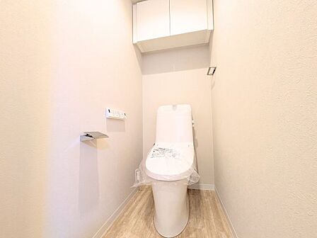 上部吊戸棚を備えた清潔感あふれるトイレ。トイレットペーパーなどをすっきり収納しておけます。