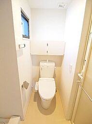 多機能便座付のトイレです。後ろには開き戸の収納スペースがあり、小さいですが採光と換気に役立つ窓もあります。