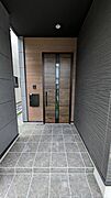 木目調のドアと重厚感のあるタイルが、邸宅の品格を醸し出すお洒落な玄関アプローチ。屋根（軒）があるため雨の日でも濡れにくく、鍵の出し入れや荷物の整理もスムーズ。毎日の帰宅が楽しみになる洗練された空間です