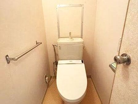 シンプルで無駄のないトイレ空間です。手すりが設置されており使い勝手に配慮されています。便器上部には手洗いスペースも備えられています。落ち着いた色合いの内装が特徴的です。清潔感のある印象を受けます。