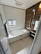 窓が設けられており換気しやすいバス空間です。浴槽は足を伸ばせる広さがあります。ダークブラウンのアクセントパネルが落ち着いた印象を与えます。洗い場は手すりが設置されており利便性にも配慮されています。