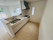 明るい室内に調和するナチュラルカラーのキッチンです。使いやすいシンクとコンロが並び収納力にも配慮されています。横長の窓からは光が差し込み空間を開放的に感じられます。
