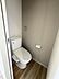 トイレ：シンプルなデザインのトイレで清掃がしやすい仕様です。落ち着いた色味の壁と床が空間に調和しています。コンパクトながらも必要な設備が整っています。ペーパーホルダーやタオルリングも設置されています。