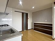 ダークブラウンの木目調が美しいシステムキッチン。背面には同デザインの収納カウンターを備え、食器や家電もすっきり片付きます。アクセントクロスがお洒落な空間を演出。機能性とデザイン性を兼ね備えた空間です。
