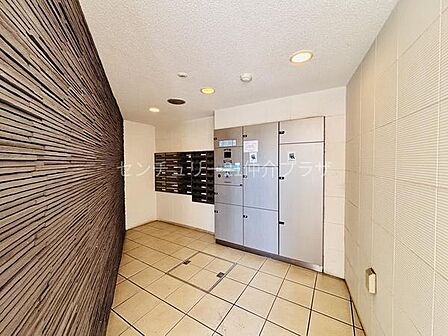 宅配ボックスと郵便受けが設置されているエントランススペースです。照明付きで明るい空間が広がります。清潔感のあるタイル床が印象的です。壁面のデザインも特徴的です。