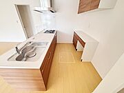 明るい色合いの床と木目調の収納が調和したキッチンです。シンプルなデザインで清潔感があります。シンクやコンロの配置が使いやすい印象です。壁面にも収納スペースが確保されています。無駄のない空間設計です。