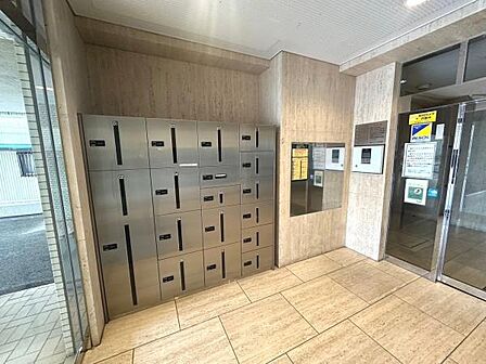 マンションのエントランスに宅配ボックスが設置されています。荷物の受け取りが便利になります。共用部分が清潔に保たれています。エントランスにはオートロックも見受けられます。
