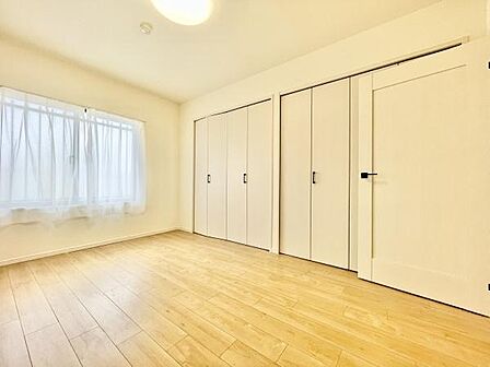 明るい印象の洋室です。床にはナチュラルな色合いのフローリングが使われています。窓からの光がしっかりと入る空間です。収納扉が複数ありすっきりとした印象を与えます。