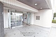 広々としたエントランスが印象的です。ガラス扉が開放感を演出し明るい雰囲気です。タイル貼りの外観が清潔感を感じさせます。エントランス横には緑も配置されています。雨の日も安心の屋根付きスペースです。