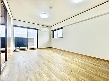 リビングには大きな窓があり室内が明るく開放感があります。フローリングの色合いが落ち着いた雰囲気を演出しています。エアコンが設置されており快適に過ごせます。バルコニーへの出入りもスムーズです。