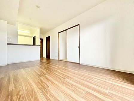 リビングは明るい色合いのフローリングが特徴です。広々とした空間で開放感が感じられます。室内はシンプルな内装でさまざまな家具との調和が期待できます。キッチンとのつながりもあり使いやすい配置です。
