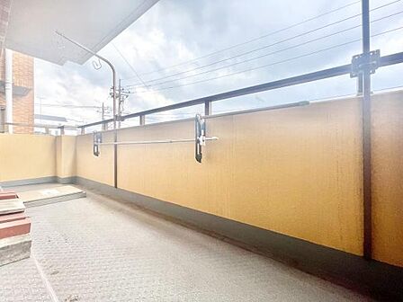 開放感のある広々としたバルコニーです。高い柵でしっかりとプライバシーが確保されています。洗濯物を干す設備も備わっています。屋根付きなので急な天候変化にも対応できます。安心してご利用いただける空間です。