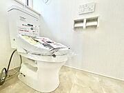 明るい色合いの床と壁で清潔感を感じるトイレです。使いやすいペーパーホルダーやリモコンも設置されています。新しい設備が印象的な空間です。収納スペースも確保されています。全体がすっきりとしたデザインです。