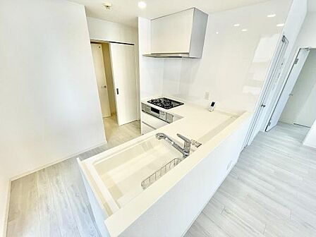 明るく開放的なキッチンは使いやすいレイアウトです。白を基調とした空間が清潔感を演出します。収納スペースも充実しています。床や壁も統一感があります。コンロやシンクが使いやすい位置に配置されています。