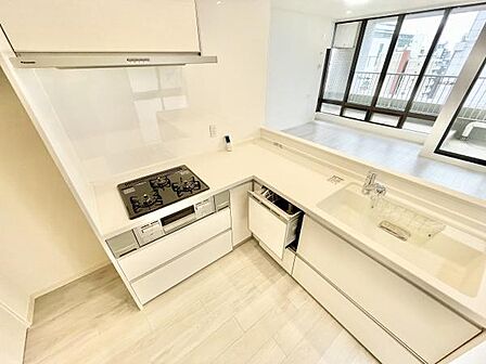 キッチン全体が明るい色合いで統一されており空間が広く感じられます。三口コンロや広めのシンクが備わっていて使い勝手の良さが印象的です。大きな窓からリビングが見渡せる開放的な設計です。