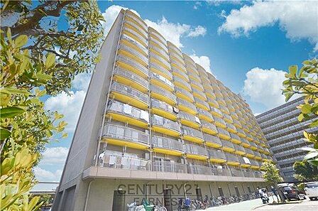 黄色のバルコニーが印象的な外観です。青空と調和したデザインが魅力となっています。高層の建物で見晴らしも期待できます。駐輪場や周辺の緑も整えられています。アクセスに便利な立地です。