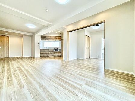 明るい色合いのフローリングが空間を広く感じさせます。開放感のある間取りが魅力的です。キッチンとのつながりが便利なリビングです。シンプルなデザインでインテリアが映えます。天井照明も配置されています。