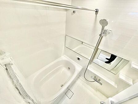 白を基調とした清潔感のあるバスルームです。大きなミラーが空間を広く見せます。浴槽とシャワーが一体となったデザインが特徴的です。収納棚もついておりシンプルな使い勝手が魅力です。