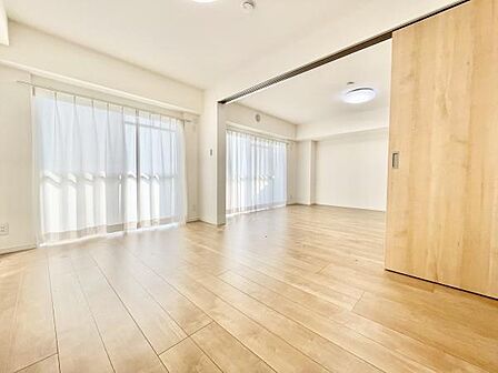 大きな窓からたっぷりと自然光が差し込む寝室です。明るく開放感のある空間が特徴です。床の木目が温かみを感じさせます。引き戸によって空間の使い方が調整できます。余裕のあるレイアウトが可能です。