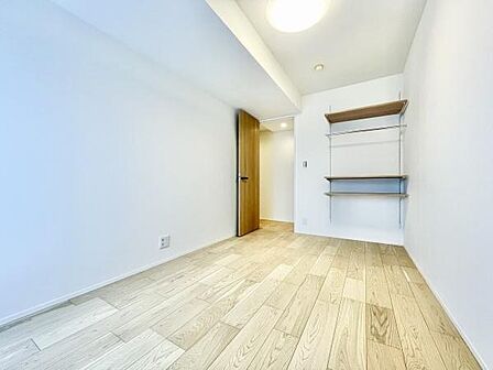 明るい色合いのフローリングが特徴の寝室です。室内がすっきりとした印象で壁面には実用的な棚も備え付けられています。入口付近まで自然な光が広がりシンプルなデザインで使いやすい空間です。