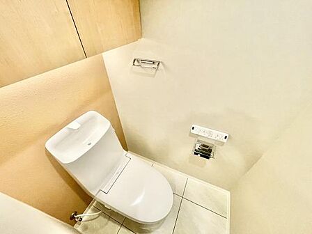シンプルなデザインのトイレが設置されています。壁付けのリモコンが使いやすい仕様です。床や壁の色味が明るく清潔感があります。収納スペースも設けられており日常の使い勝手に配慮されています。
