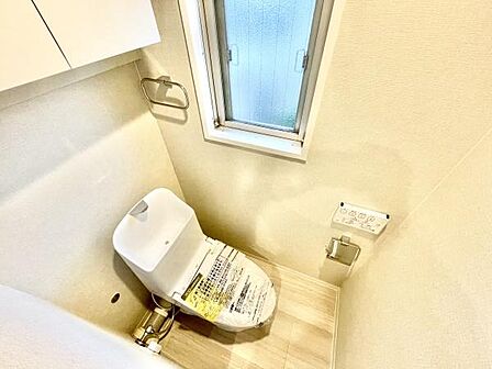 明るい採光のあるトイレです。壁に設置された収納スペースが空間を有効活用しています。窓があるため換気もしやすく衛生的です。床は清潔感のある色合いでお手入れもしやすい設計です。