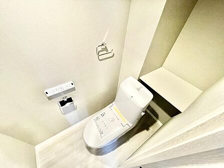 ホワイトを基調とした明るいトイレ空間です。収納スペースが備わっており使いやすさに配慮されています。ペーパーホルダーやリモコン式の操作パネルも設置されています。清潔感あふれる印象です。