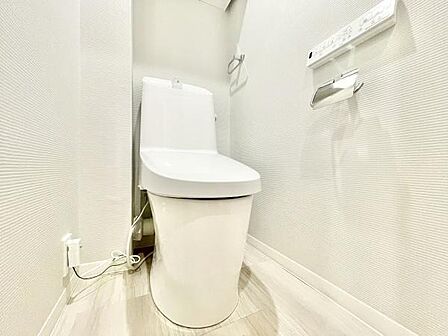 清潔感のあるホワイトを基調としたトイレです。コンパクトな空間設計で使いやすさが感じられます。壁付けリモコンやペーパーホルダーも設置されています。床や壁のトーンが統一され明るい印象です。